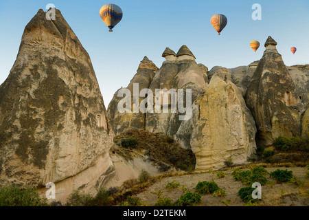 Cave homes in fairy chimneys of Cavusin Cappadocia Goreme National Park Nevsehir Turkey with hot air balloons Stock Photo