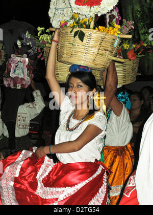 colorful procession in Oaxaca de Juarez, Mexico on the night of January 31st, 2013, celebrates Our Lady of the Candles; Nuestra Señora de la Candelaria. Pretty dancer in bright traditional costume whirls across the street carrying a basket of fresh flowers on her head. Stock Photo