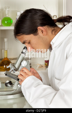Young lab worker in lab coat using a microscope Stock Photo