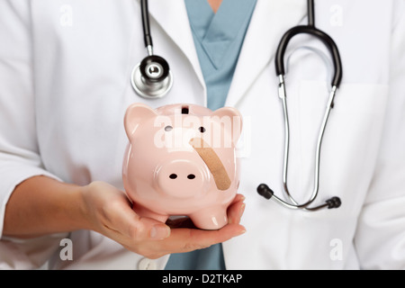 Female Doctor with Stethoscope Holding Piggy Bank with Bandage on Face. Stock Photo