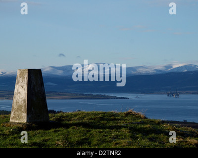 Looking past a Trig point over the Cromarty Firth to Ben Wyvis in the Scottish Highlands, with Oil Rigs moored near Invergordon. Stock Photo