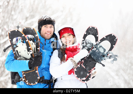 Portrait of young smiling active mixed race winter couple holding snowshoes hiking in snow Stock Photo