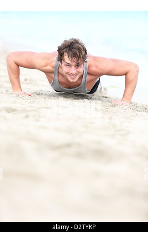 Portrait of young handsome Caucasian man in his twenties doing push-ups on beach Stock Photo