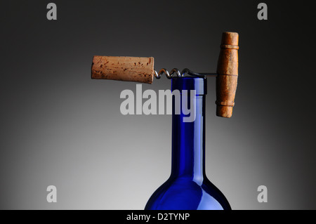 Closeup of an antique corkscrew with cork attached resting on top of a blue wine bottle. Stock Photo