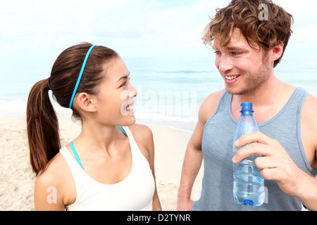 Multiracial couple talking, relaxing and smiling after running on beach Stock Photo