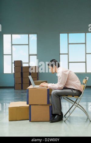 Businessman using a laptop in a warehouse with cardboard boxes Stock Photo
