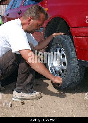 Adult man sitting on ground change wheel of red car Stock Photo