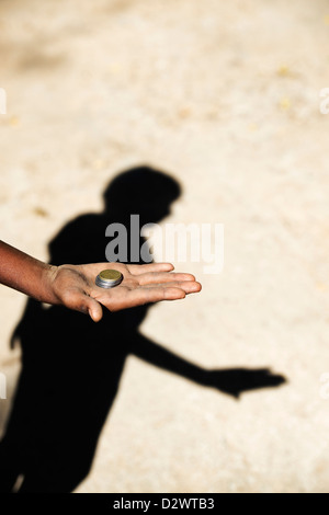 Poor Indian childs hand stretched out begging holding rupee coins and shadow. India Stock Photo