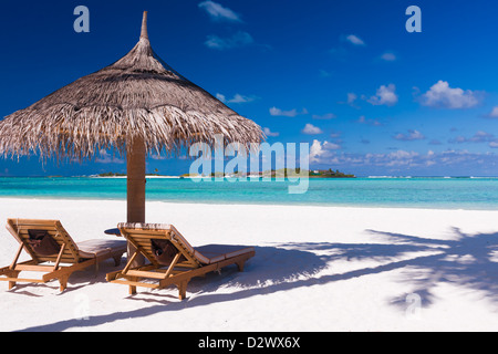 Two chairs and umbrella on a beach with shadow from palm tree Stock Photo