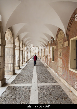 Lone figure walking along the outside arcade of the 16th century Casa de Oficios y Caballeros de Aranjuez Spain Stock Photo