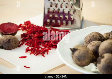 Beetroot on a cuttingboard, Some of the beetroots are grated and there is a grater in background. Stock Photo