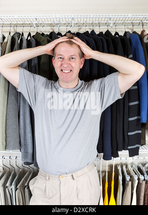 Vertical portrait of mature Caucasian man in walk-in closet showing frustration with hands behind head while pulling his hair Stock Photo