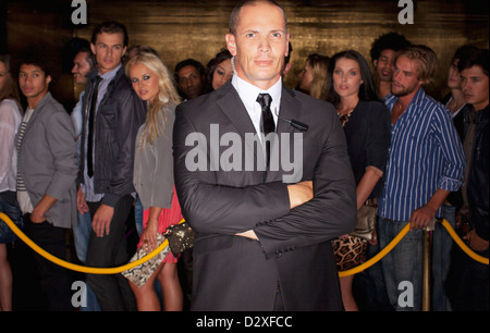 Portrait of serious bouncer with arms crossed in front of queue at nightclub Stock Photo