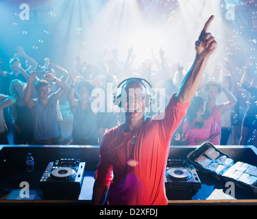 Portrait of enthusiastic DJ with arm raised and people on dance floor in background Stock Photo