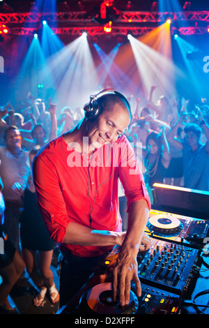 DJ at turntable with crowd on dance floor in background Stock Photo