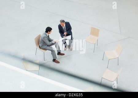 Businessmen reviewing paperwork in circle of chairs Stock Photo