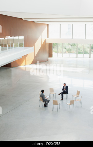 Businessmen sitting at circle of chairs in modern lobby Stock Photo