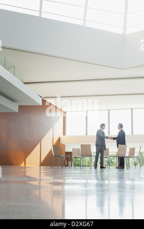 Businessmen shaking hands at circle of chairs in lobby Stock Photo