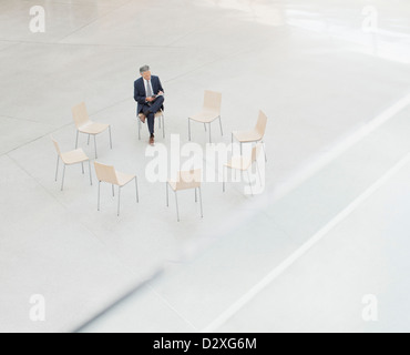 Businessman reviewing paperwork at circle of chairs in lobby Stock Photo