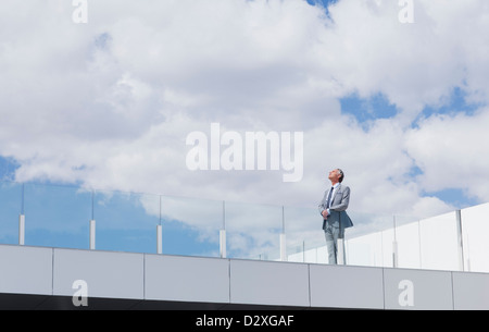 Pensive businessman looking up at sky on rooftop balcony Stock Photo
