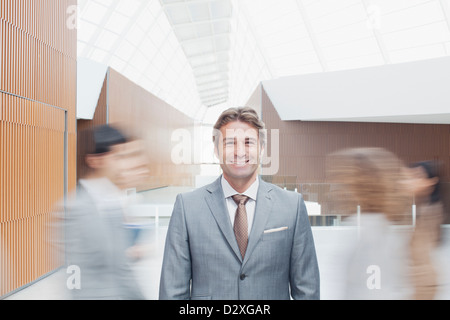 Portrait of confident businessman with co-workers rushing by in lobby Stock Photo