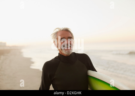 Older surfer carrying board on beach Stock Photo