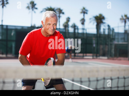 Older man playing tennis on court Stock Photo