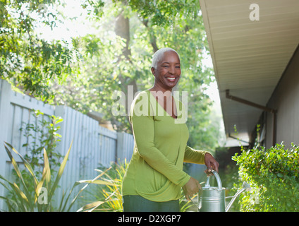 Older woman watering plants in backyard Stock Photo