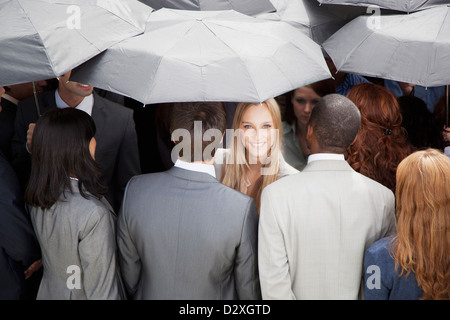 Portrait of smiling businesswoman surrounded by crowd with umbrellas Stock Photo
