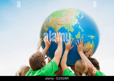 Team in green t-shirts lifting globe overhead Stock Photo