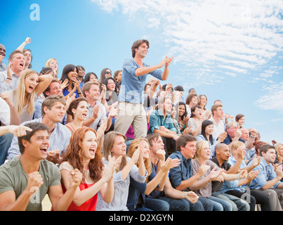 Man standing and clapping among cheering crowd Stock Photo