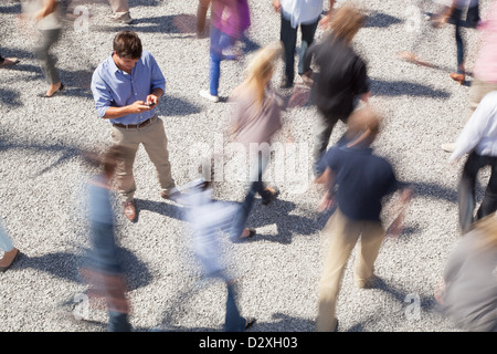 Man checking cell phone among rushing crowd Stock Photo