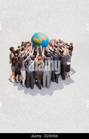 Crowd of business people in huddle lifting globe overhead Stock Photo