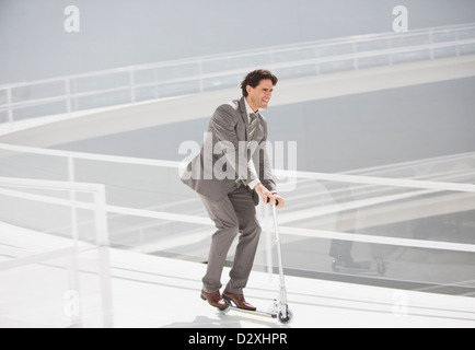 Businessman riding scooter down walkway Stock Photo