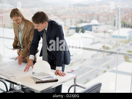 Architects reviewing blueprints in office overlooking city Stock Photo