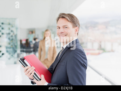 Portrait of smiling businessman holding paperwork in corridor Stock Photo