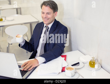 Smiling businessman drinking coffee and using laptop in restaurant Stock Photo