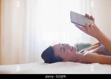 Smiling woman laying on bed and using digital tablet Stock Photo