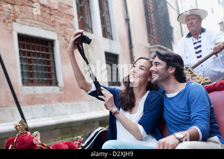 Smiling couple taking self-portrait with digital camera in gondola on canal in Venice Stock Photo