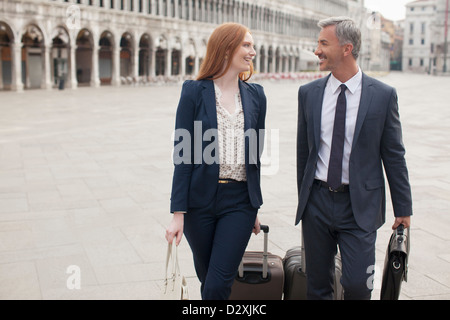 Smiling businessman and businesswoman pulling suitcases through St. Mark’s Square in Venice Stock Photo