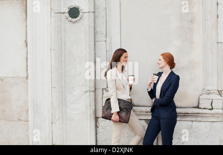 Smiling businesswomen drinking coffee and talking against building wall Stock Photo