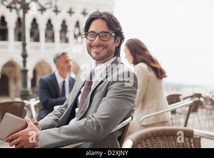 Portrait of smiling businessman holding digital tablet at sidewalk cafe in Venice Stock Photo