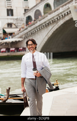 Portrait of smiling businessman with coffee walking along canal in Venice Stock Photo