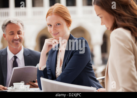 Portrait of smiling businesswomen working with co-workers at sidewalk cafe Stock Photo