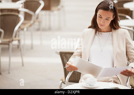 Serious businesswoman reading paperwork at sidewalk cafe Stock Photo