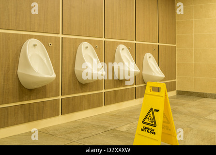 Row of urinals and wet floor sign in toilets Stock Photo