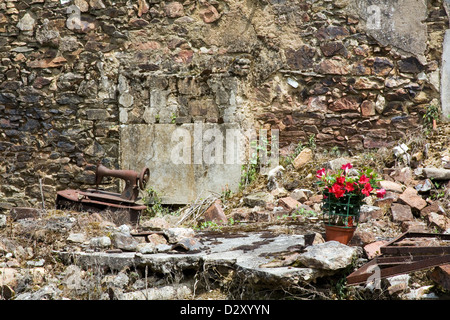 Flowers left for remembrance in a burnt out destroyed cottage in the French village Oradour-sur-Glane. A rusty sewing machine. Stock Photo