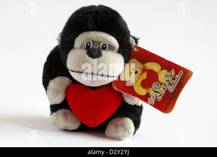 Chimp holding red heart soft cuddly toy isolated on white background - ideal present gift for Valentine day Stock Photo