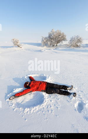 Woman in red coat making a snow angel, Wales, UK Stock Photo