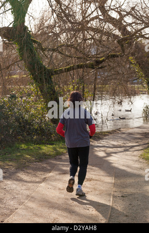 back view of female jogger on path by lake in winter sunshine Stock Photo